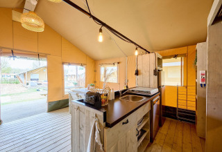Interior de la tienda safari en Camping Si-Es-An, Países Bajos, con cocina y zona de comedor.
