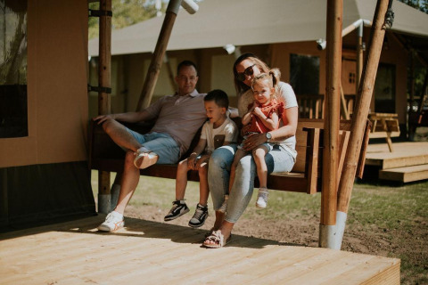 Familia sentada junta en el porche de una tienda safari en Camping Si-Es-An, Países Bajos, disfrutando.