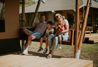 Familia sentada junta en el porche de una tienda safari en Camping Si-Es-An, Países Bajos, disfrutando.