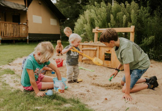 Kinder spielen im Sandkasten vor einem Safari-Zelt-Lodge auf Camping Si-Es-An in den Niederlanden.