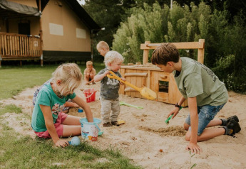 Børn leger i sandkassen foran en safari-telt lodge på Camping Si-Es-An i Holland, med legetøj.