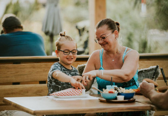 Mor og barn deler et måltid udendørs på Safari teltet ved Camping Si-Es-An, Holland, og smiler sammen.