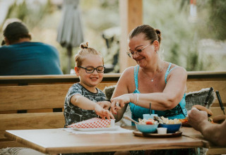 Madre e hijo disfrutan de una comida juntos en una tienda safari de Camping Si-Es-An, Países Bajos, sonriendo.