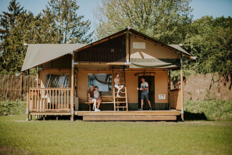Famiglia si rilassa davanti alla Ranger Lodge al Camping Si-Es-An nei Paesi Bassi, circondata dal verde.