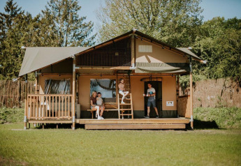 Famiglia si rilassa davanti alla Ranger Lodge al Camping Si-Es-An nei Paesi Bassi, circondata dal verde.