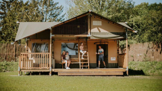 Family relaxing outside Ranger Lodge at Camping Si-Es-An in the Netherlands, surrounded by greenery.