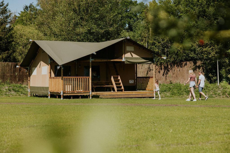 Family walking past the Ranger lodge at Camping Si-Es-An in the Netherlands, surrounded by lush nature.