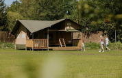 Familia paseando junto a la Ranger lodge en Camping Si-Es-An, Países Bajos, rodeados de naturaleza verde.