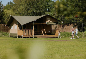 Familie går forbi Ranger-lodge på Camping Si-Es-An i Holland, omgivet af natur og frodigt grønt.