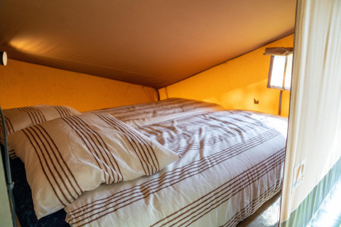 Cama acogedora con sábanas a rayas en la Ranger lodge del Camping Si-Es-An en los Países Bajos.