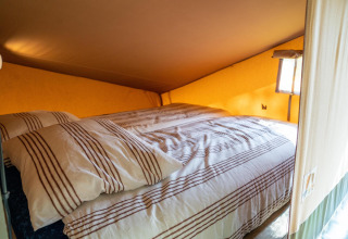 Cama acogedora con sábanas a rayas en la Ranger lodge del Camping Si-Es-An en los Países Bajos.