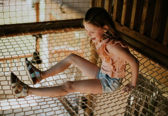 Meisje speelt op touwnet in Ranger Lodge bij Camping Si-Es-An in Nederland, in zomerse outfit en sandalen.