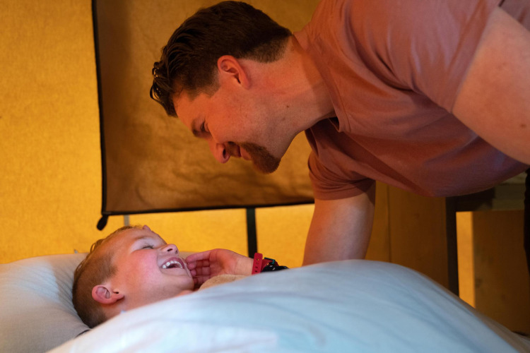 A father leans over his laughing son in bed at the Ranger Lodge at Camping Si-Es-An in the Netherlands.