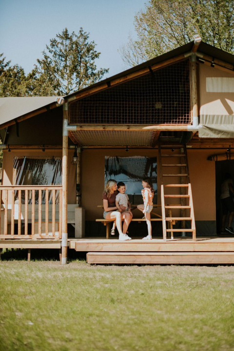 Gezin geniet op het terras van de Ranger lodge bij Camping Si-Es-An in Nederland op een zonnige dag.