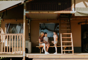 Family enjoys time on the porch of the Ranger lodge at Camping Si-Es-An in the Netherlands on a sunny day.