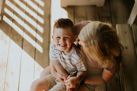 Bambino sorridente in braccio alla madre su una veranda di legno al Ranger lodge, Camping Si-Es-An, Paesi Bassi.