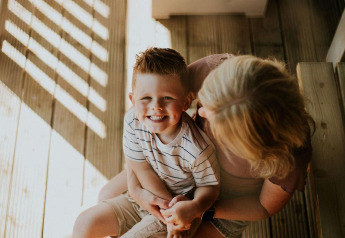 Garçon souriant assis sur les genoux de sa mère sur la terrasse en bois du Ranger lodge à Camping Si-Es-An, Pays-Bas.
