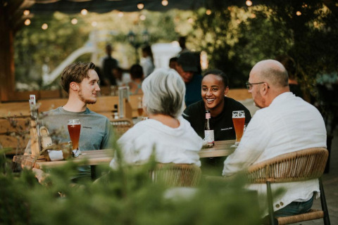 Cuatro personas disfrutan de bebidas y conversación al aire libre en Ranger lodge en Camping Si-Es-An, Países Bajos.