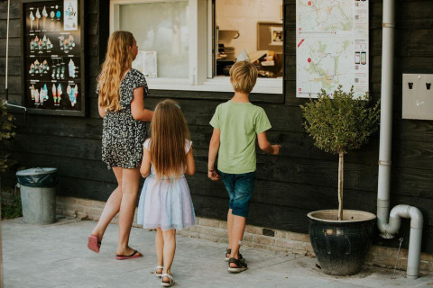 Tres niños esperan frente a un kiosco de helados en un alojamiento glamping, listos para pedir algo.