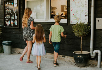 Tre bambini davanti a un chiosco dei gelati in un campeggio glamping, pronti a ordinare un gelato.