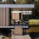 Moderne glampingaccommodatie boven water met veranda, houten gevelbekleding en uitzicht op natuur.