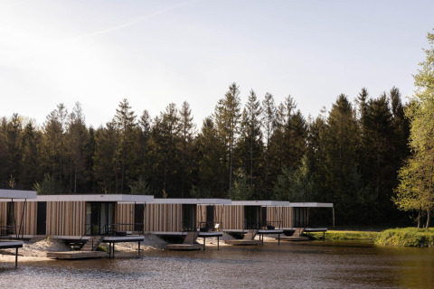 Cabañas de glamping modernas sobre pilotes junto a un lago, rodeadas de bosque, ideal para relajarse.