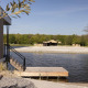Cabaña de madera junto a un lago con embarcadero, playa y tienda glamping rodeada de bosque.