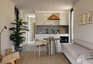 Modernes Glamping-Unterkunftsinterieur mit Küche, Esstisch, gemütlichem Sofa und Pflanzen dekoriert.