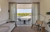 Sala de estancia minimalista en glamping con terraza y vistas al lago y bosque a través de puertas de cristal.