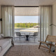 Minimalistische woonkamer in een glampingaccommodatie met uitzicht op het meer en bos via glazen deuren.
