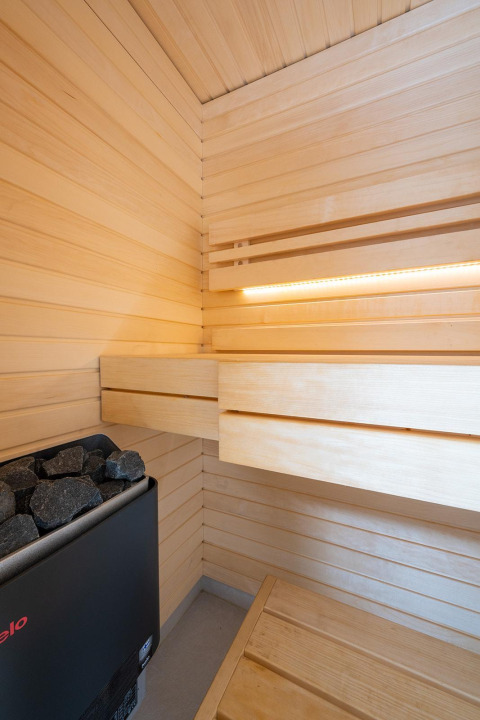 Vista interior de una sauna moderna con paneles de madera y piedras en Waterlodge Sauna, Resort de Parel, Países Bajos.