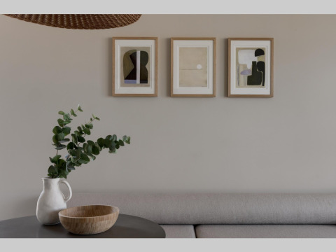 Zona de estar minimalista en alojamiento glamping, con tres cuadros abstractos, jarrón y cuenco de madera.