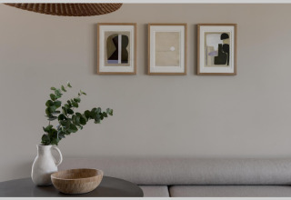 Minimalistisch salon bij glamping, met drie abstracte kunstwerken, een vaas met groen en een houten kom.