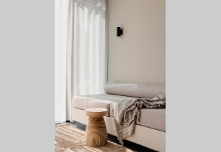 Alojamiento glamping iluminado con sofá cómodo, mesa de madera, manta suave y cortinas translúcidas.