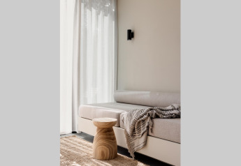 Alloggio glamping luminoso con divano accogliente, sgabello in legno e tende leggere vicino alla finestra.