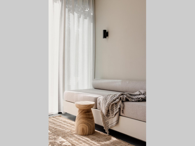 Bright glamping accommodation with cozy sofa, wooden stool, soft throw, and sheer curtains on window.