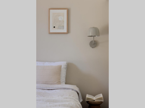 Et hyggeligt glampingværelse med en komfortabel seng, væglampe, kunst på væggen og åben bog på bordet.