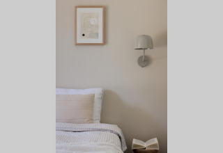 Knusse glampingkamer met comfortabel bed, wandlamp, kunstwerk en open boek op een houten tafeltje.