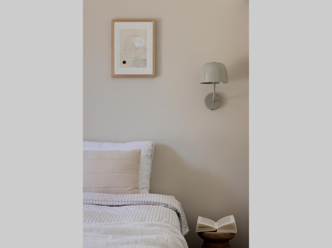 Gemütliches Glamping-Zimmer mit Bett, Wandlampe, moderner Kunst an der Wand und geöffnetem Buch auf Tisch.