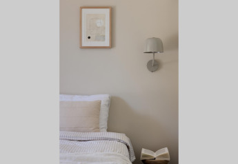 Cozy glamping accommodation with a bed, wall lamp, minimalist artwork, and an open book on a wooden table.