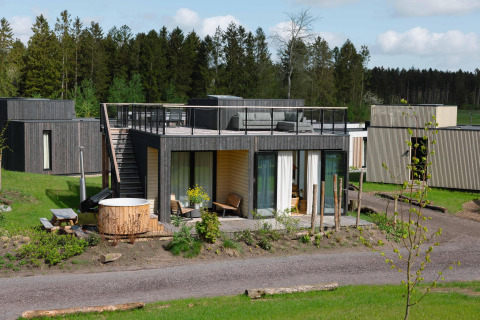 Modern lodge with roof terrace and outdoor hot tub at Resort de Parel, Netherlands, surrounded by trees.