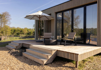 Terrazza in legno di un lodge con due sedie, ombrellone e bicchieri, davanti a grandi porte a vetri.