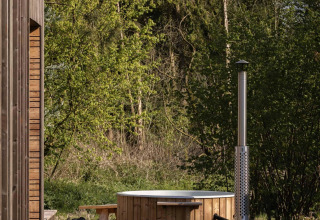 Træbadekar med skorsten ved en hytte i naturen på Resort de Parel i Nederlandene omringet af træer.