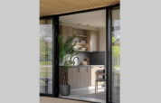 Moderne lodgekeuken met houtlook kasten, kamerplant en grote glazen deuren met uitzicht op de natuur.