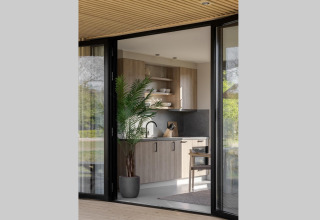 Moderne lodgekeuken met houtaccenten, kamerplant en grote glazen deuren met zicht op de buitenomgeving.