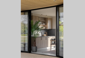Moderne lodgekeuken met houtaccenten, kamerplant en grote glazen deuren met zicht op de buitenomgeving.