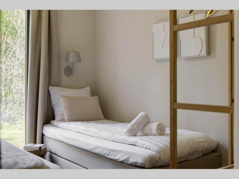 Habitación de lodge moderna con cama individual, almohadas, toallas enrolladas y vista al exterior verde.