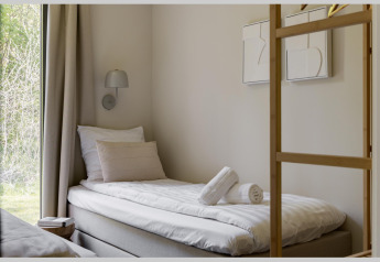 Habitación de lodge moderna con cama individual, almohadas, toallas enrolladas y vista al exterior verde.