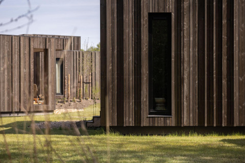 Photo extérieure d’un lodge avec façades en bois moderne, fenêtres étroites et pelouse verte au premier plan.