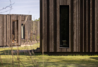 Photo extérieure d’un lodge avec façades en bois moderne, fenêtres étroites et pelouse verte au premier plan.